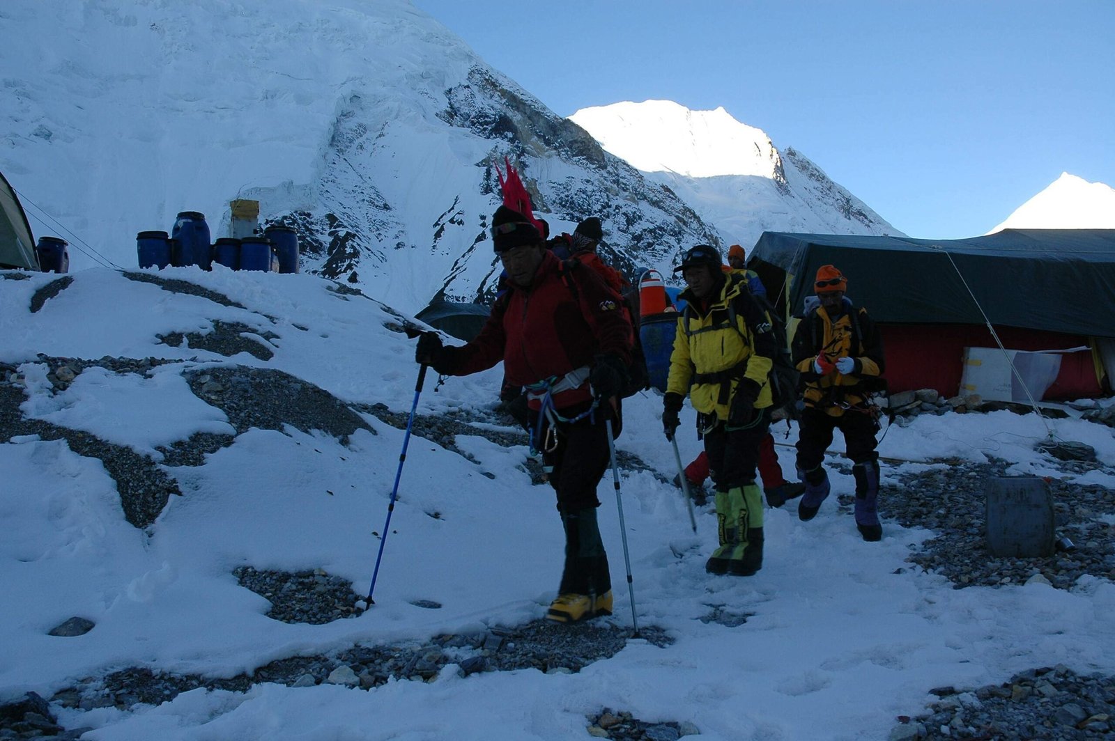 Trekkers standing at K2 Base Camp with the towering peak of K2 in the background, surrounded by rugged glaciers and snow-capped mountains.