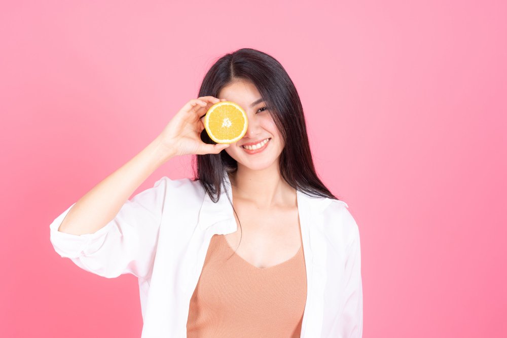 Asian girl with long black hair, holding half an orange.